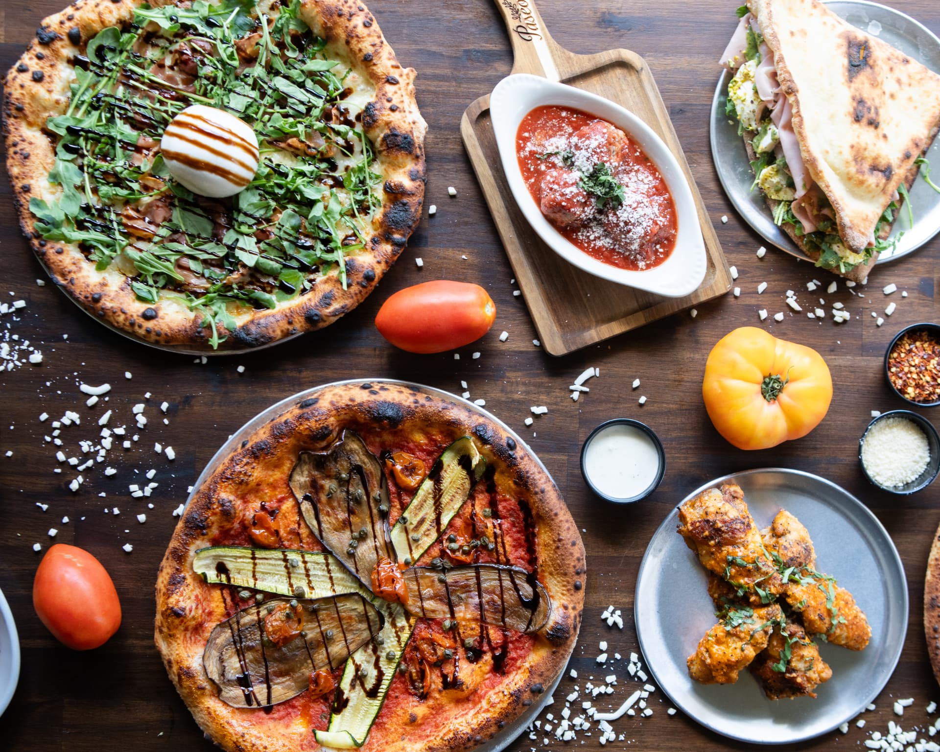 Paseo pizzas, panuozzo, meatballs and wings arranged across a dining table