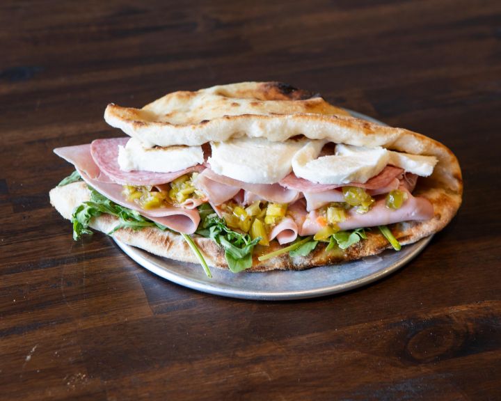 Italian panuozzo with salami, mortadella, fresh mozzarella, giardiniera and mixed greens