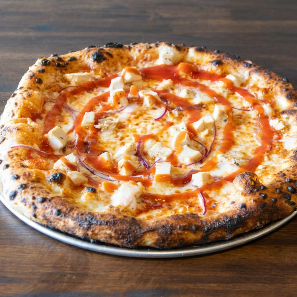 Neapolitan-style pizza with charred crust, melted cheese, diced chicken, red onion, and tomato sauce on a metal tray.